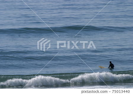 A surfer lying on his surfboard paddles over an approaching wave on a beach in Portugal on the Atlantic Ocean A surfer lying on his surfboard paddles over an approaching wave on a beach in Portugal on the Atlantic Ocean 75013440
