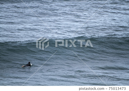 A surfer lying on his surfboard paddles over an approaching wave on a beach in Portugal on the Atlantic Ocean 75013473