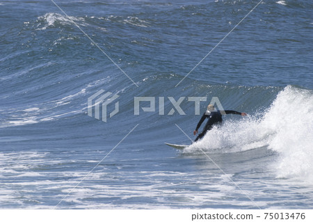 A surfer sportingly rides down a wave on a beach in Portugal on the Atlantic Ocean A surfer sportingly rides down a wave on a beach in Portugal on the Atlantic Ocean 75013476
