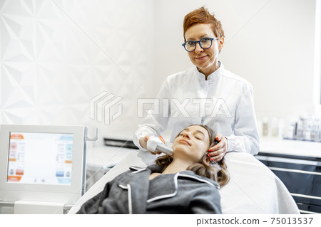 Woman on ultrasound face lifting procedure in cosmetology salon Woman on ultrasound face lifting procedure in cosmetology salon 75013537