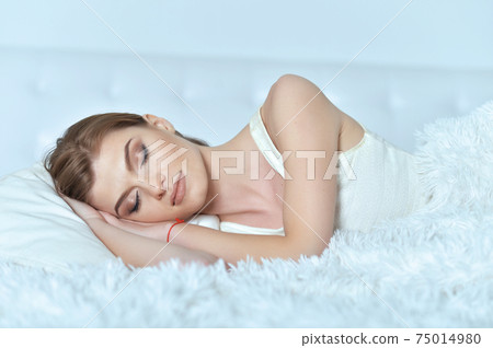 Beautiful young woman lying on soft bed Beautiful young woman lying on soft bed 75014980