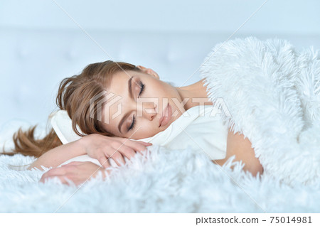 Beautiful young woman lying on soft bed Beautiful young woman lying on soft bed 75014981
