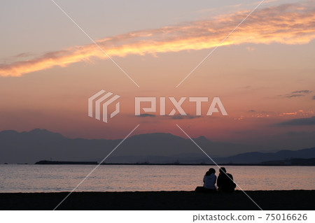Two people staring at the sunset at the beach Two people staring at the sunset at the beach 75016626