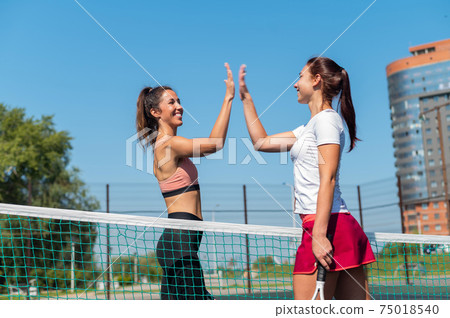 Two Caucasian women in sportswear greeting before a tennis match on an outdoor court. Players give a high five before the game. 75018540