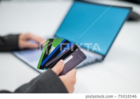 Close-up of female hands with many plastic credit cards. A woman holds several bank debit cards and makes purchases on the Internet on a laptop. The concept of online shopping with a loan. 75018546