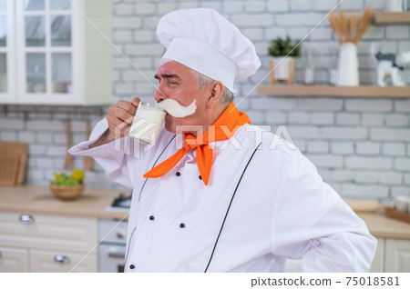 A friendly elderly milkman with a glass of milk. Portrait of a male farmer with a bushy mustache. 75018581