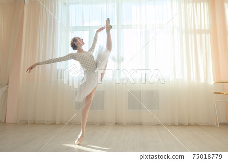 Beautiful ballerina in body and white tutu is training in a dance class. Young flexible dancer posing in pointe shoes. 75018779