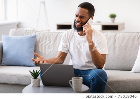 Black Man Talking On Phone Having Problem With Laptop Indoor Black Man Talking On Phone Having Problem With Laptop Indoor 75019046