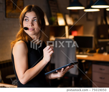 Beautiful caucasian woman in a headset is holding a digital tablet. Portrait of a business woman in the office 75019050