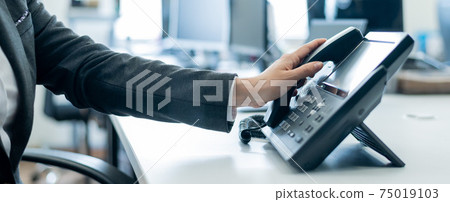 Close-up of a female employee's hand on a landline phone. Woman picks up a push-button telephone at the workplace in the office Close-up of a female employee's hand on a landline phone. Woman picks up a push-button telephone at the workplace in the office 75019103