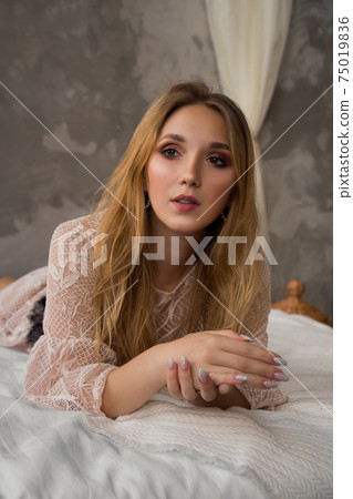 Vertical portrait of a woman lying on bed. Light interior Vertical portrait of a woman lying on bed. Light interior 75019836
