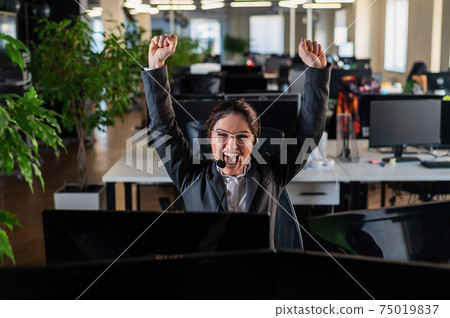 Business woman rejoices at work success. The female call center operator raised her hands in happiness at her desk 75019837