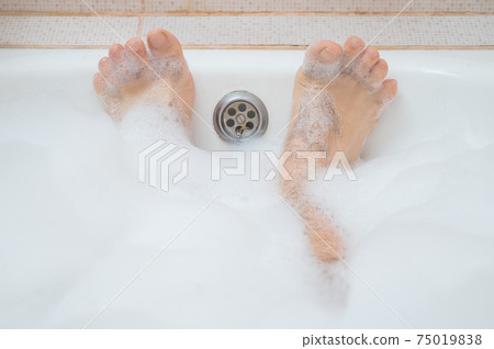 Funny picture of a man taking a relaxing bath. Close-up of male feet in a bubble bath Funny picture of a man taking a relaxing bath. Close-up of male feet in a bubble bath 75019838