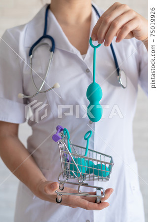 A faceless gynecologist puts a set of vaginal balls into a miniature shopping cart. The doctor holds a mini trolley and device for the muscles of the pelvic floor. Female health concept. Kegel toy A faceless gynecologist puts a set of vaginal balls into a miniature shopping cart. The doctor holds a mini trolley and device for the muscles of the pelvic floor. Female health concept. Kegel toy 75019926