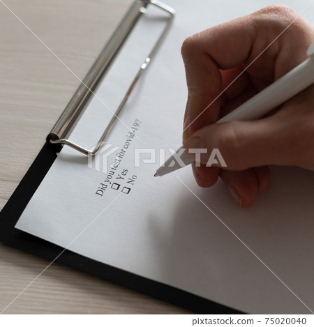 Unrecognizable woman puts a daw in the questionnaire. A close-up of a female hand answering about a a covid-19 question. marking in a checkbox 75020040
