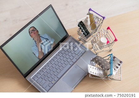 Online medicine and pharmacy concept. A female doctor conducts an online consultation and recommends medications. Mini trolley with tablets at the laptop. 75020191