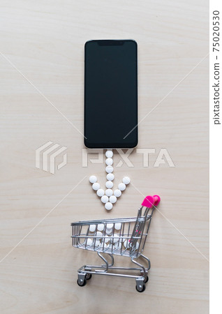 Online pharmacy concept. Buying medicine online over the phone. Delivery of pharmaceuticals. Mini trolley with capsules and a smartphone with a black blank screen. 75020530