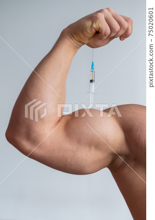 Close-up of male biceps. Unrecognizable male bodybuilder puts himself an injection of testosterone. Faceless athlete takes growth hormone. Vertical . Close-up of male biceps. Unrecognizable male bodybuilder puts himself an injection of testosterone. Faceless athlete takes growth hormone. Vertical . 75020601