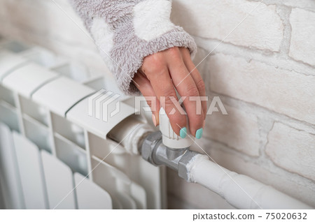 The woman opens the valve of the radiator heating. 75020632