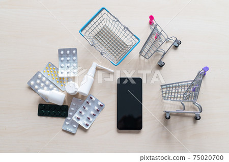 Online pharmacy concept. Buying medicine online over the phone. Delivery of pharmaceuticals. Mini trolley with different tablets, sprays, capsules and a smartphone with a black blank screen. Online pharmacy concept. Buying medicine online over the phone. Delivery of pharmaceuticals. Mini trolley with different tablets, sprays, capsules and a smartphone with a black blank screen. 75020700