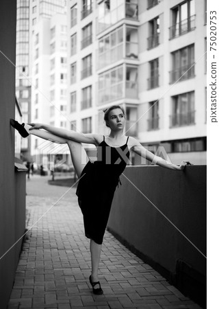 Ballerina in tutu makes an elegant pose. Beautiful young woman in black dress and pointe dancing over city background. Portrait of a gorgeous ballerina performing a dance outdoors. Black and white Ballerina in tutu makes an elegant pose. Beautiful young woman in black dress and pointe dancing over city background. Portrait of a gorgeous ballerina performing a dance outdoors. Black and white 75020753