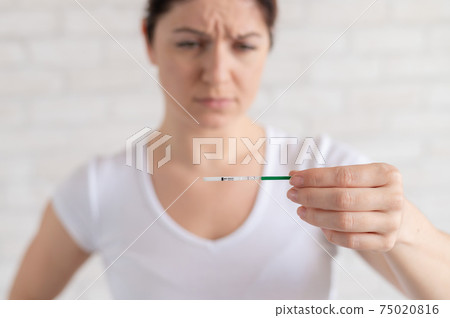 Frustrated woman shows a positive pregnancy test. Child free concept. Human chorionic gonadotropin. Two stripes. Unwanted child. 75020816