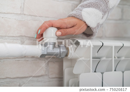 Close-up of a female hand regulating the temperature of a heating radiator 75020817