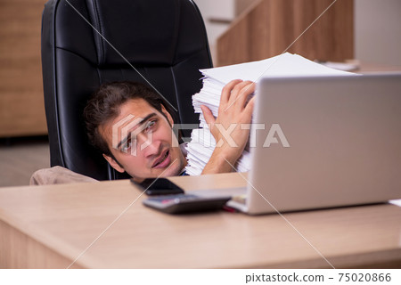 Young male employee unhappy with excessive work in the office Young male employee unhappy with excessive work in the office 75020866