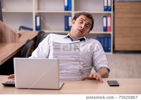 Young male employee unhappy with excessive work in the office 75020867