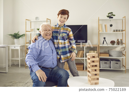 Happy smiling old gramdfather and his positive grandson boy hugging at home looking at camera Happy smiling old gramdfather and his positive grandson boy hugging at home looking at camera 75022189