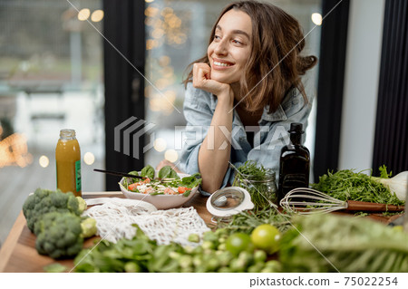 Woman eating healthy green salad in kitchen Woman eating healthy green salad in kitchen 75022254