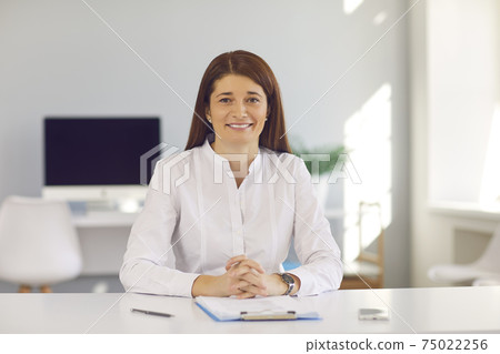 Smiling business woman or office worker looking at camera during online videocall or interview Smiling business woman or office worker looking at camera during online videocall or interview 75022256