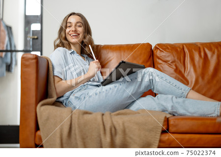 Woman working with digital tablet from home on sofa 75022374