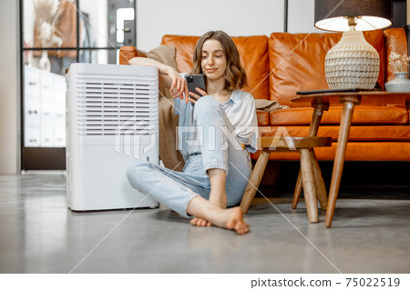 Woman sitting near air purifier and moisturizer appliance Woman sitting near air purifier and moisturizer appliance 75022519