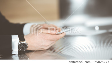 Unknown businessmen and woman sitting, working and discussing questions at meeting in modern office, close-up Unknown businessmen and woman sitting, working and discussing questions at meeting in modern office, close-up 75023273