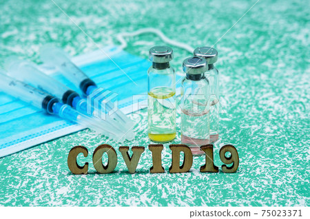 Medical ampoules, syringes, and a mask on a green background. Vaccination against covid-19. Medical ampoules, syringes, and a mask on a green background. Vaccination against covid-19. 75023371
