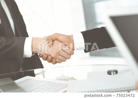 Unknown diverse business people are shaking hands finishing up meeting at the desk in office, close-up. Handshake concept 75023472