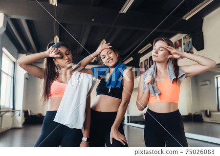 Three happy smiling positive girls after training in the gym. 75026083