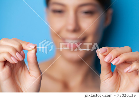 Portrait of beautiful woman cleaning teeth with dental floss 75026139