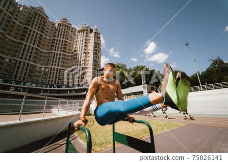 Strong man doing exercises on uneven bars in outdoor street gym. 75026141