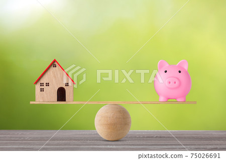 Model house on wooden seesaw balancing with piggy bank on green background. Property investment and home mortgage financial real estate advertising concept 75026691