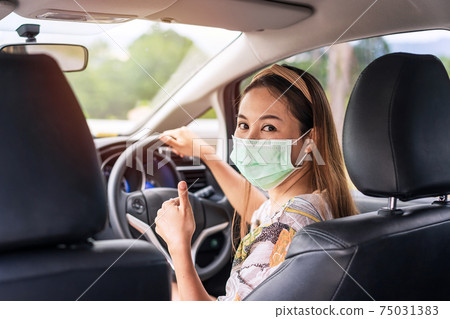 The female driver wearing surgical mask felt confident and gesturing thumbs up while traveling 75031383