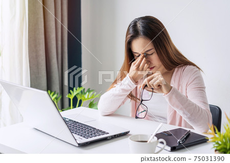Tired and stressed young asian woman feel pain eyestrain and rubbing her eyes and take off her glasses while sitting at her working place 75031390