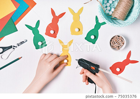 DIY Easter home decor from natural materials. Hands make garland of colored paper, twine and pom-poms DIY Easter home decor from natural materials. Hands make garland of colored paper, twine and pom-poms 75035376