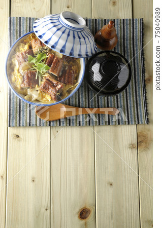 A bird's-eye view of a hot eel bowl with eel kabayaki on a place mat, a set of soup and a wooden spoon 75040989