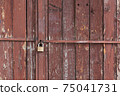 Rusty old wooden garage door painted in red with metal stel bars and padlock rural street poor neighborhood in Sofia, Bulgaria, Eastern Europe 75041731