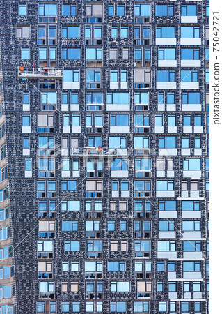 Fragment of the facade of a high-rise building under construction and its insulation using winches and mobile platforms, the concept of energy saving in residential construction. Fragment of the facade of a high-rise building under construction and its insulation using winches and mobile platforms, the concept of energy saving in residential construction. 75042721