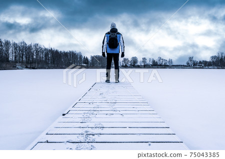 Man standing on the lake wooden pier at cold winter weather Man standing on the lake wooden pier at cold winter weather 75043385