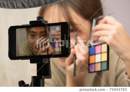 A woman shooting a make-up video on her smartphone A woman shooting a make-up video on her smartphone 75043783
