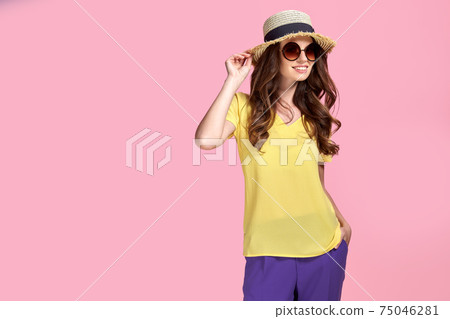 Young girl in sunglasses wearing, colorful clothes and straw hat, isolated over pink background Young girl in sunglasses wearing, colorful clothes and straw hat, isolated over pink background 75046281